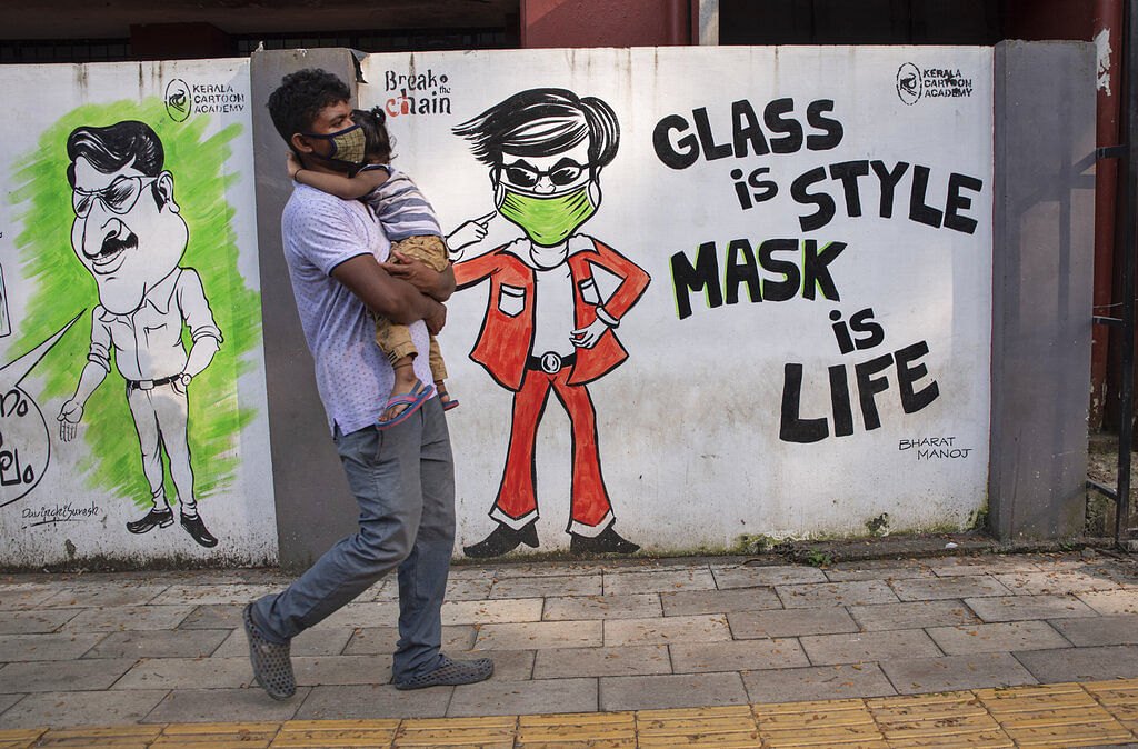 A man wearing a face mask as a precaution against the coronavirus carries a child and walks past a graffiti in Kochi, Kerala
