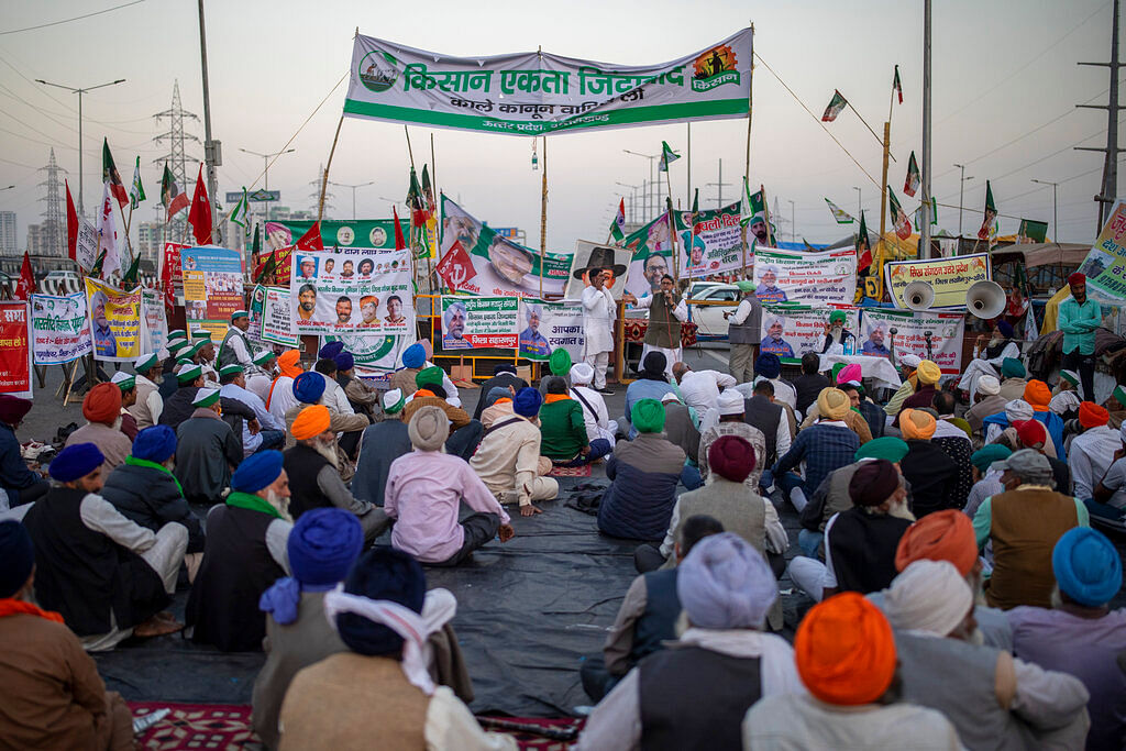 Farmers listen to a speaker, sitting in the middle of an expressway at the site of a protest against new farm laws at the Delhi-Uttar Pradesh state border, India