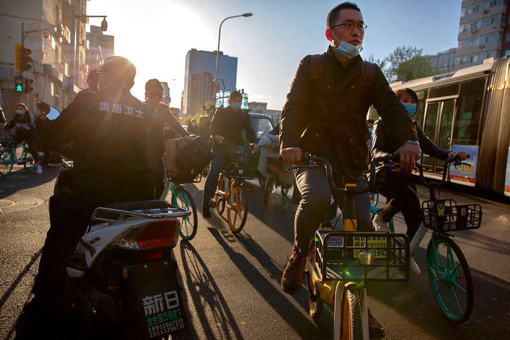People wearing face masks to prevent the spread of COVID-19 ride bicycles along a street in Beijing