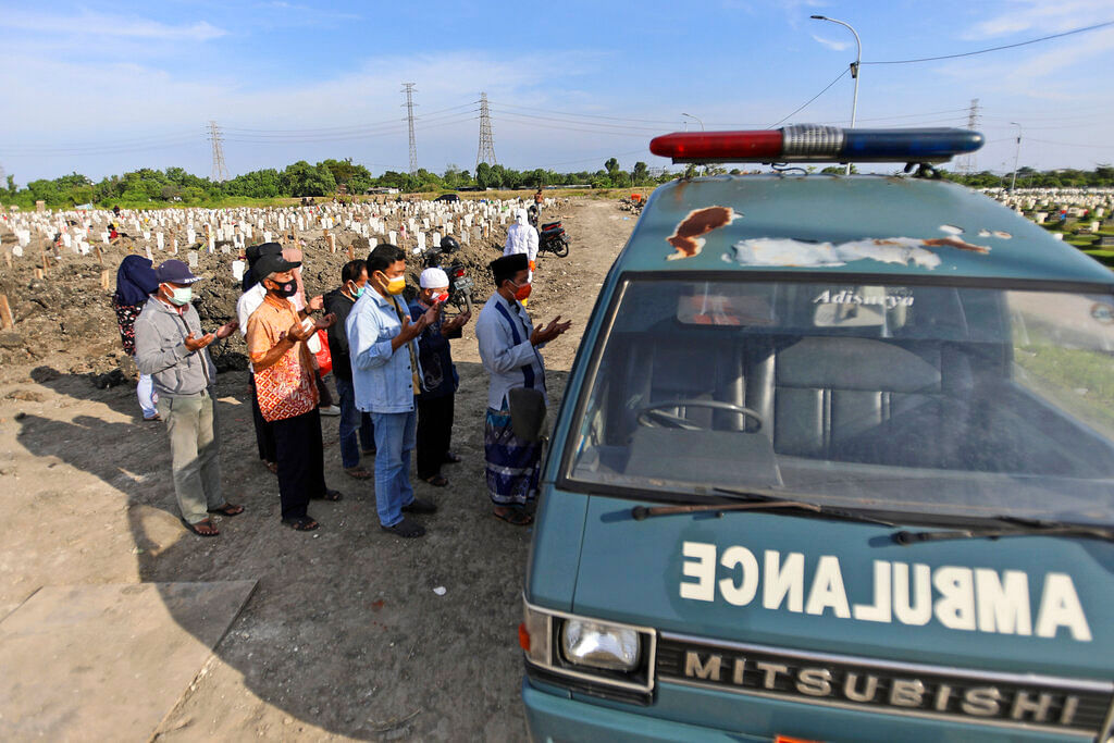 People pray outside an ambulance carrying the body of a relative who died from the coronavirus before the burial at a cemetery in Surabaya, East Java, Indonesia